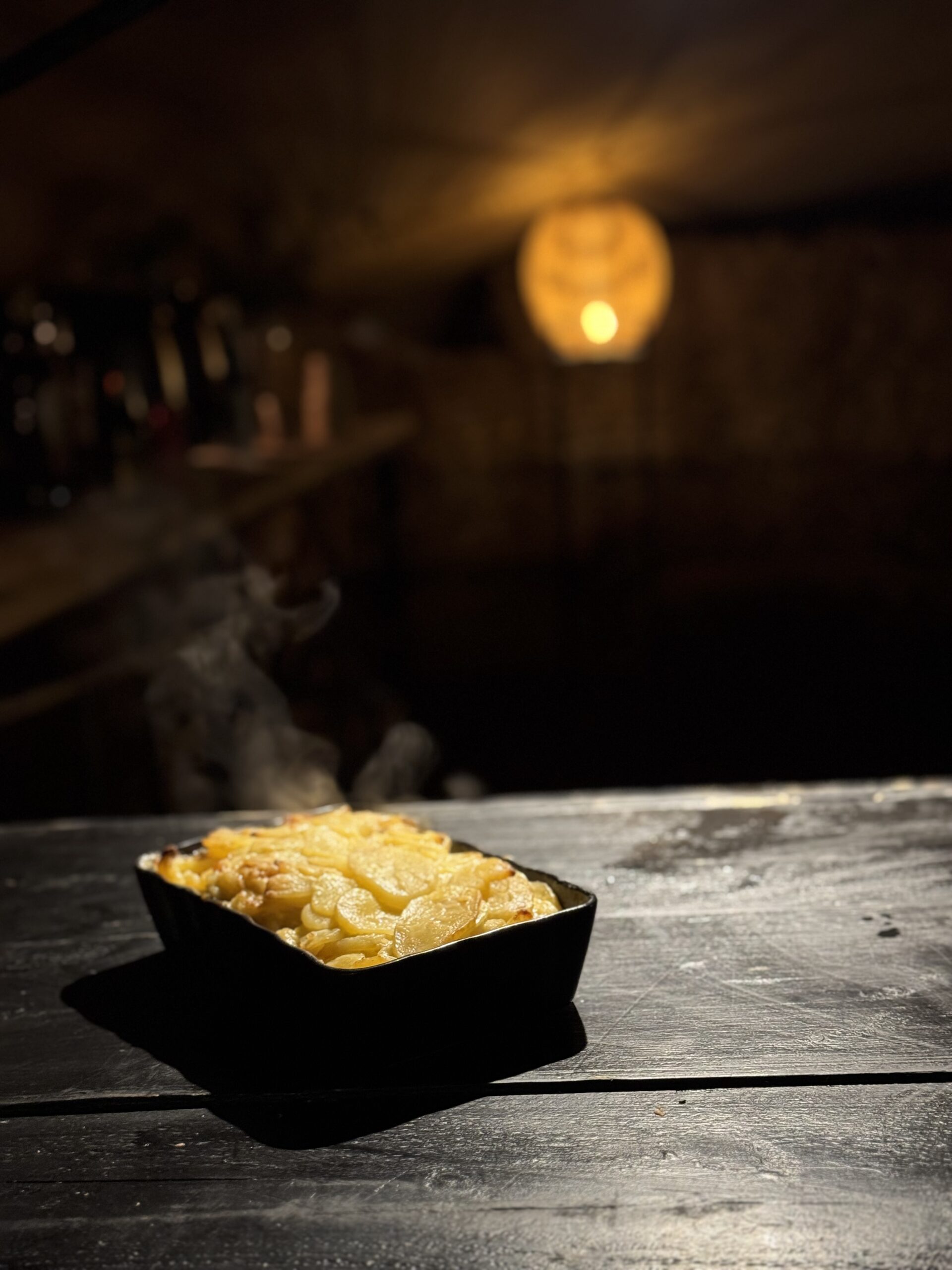 Hete aardappelgratin in een zwart ovenschaaltje met donkere achtergrond